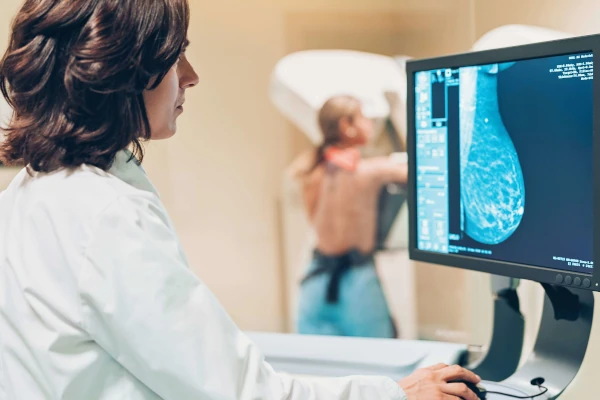 Médica realizando exame de tomografia com paciente apoiada no equipamento ao fundo.